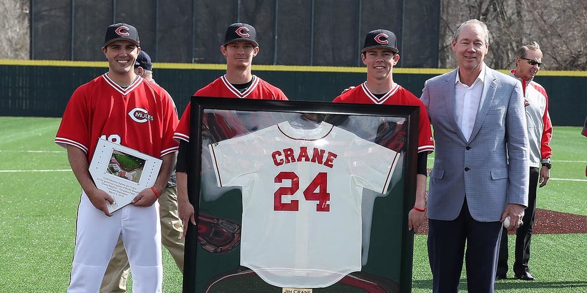 Jim Crane with three Mules players, holding the framed CRANE 24 jersey and a plaque at Crane Stadium