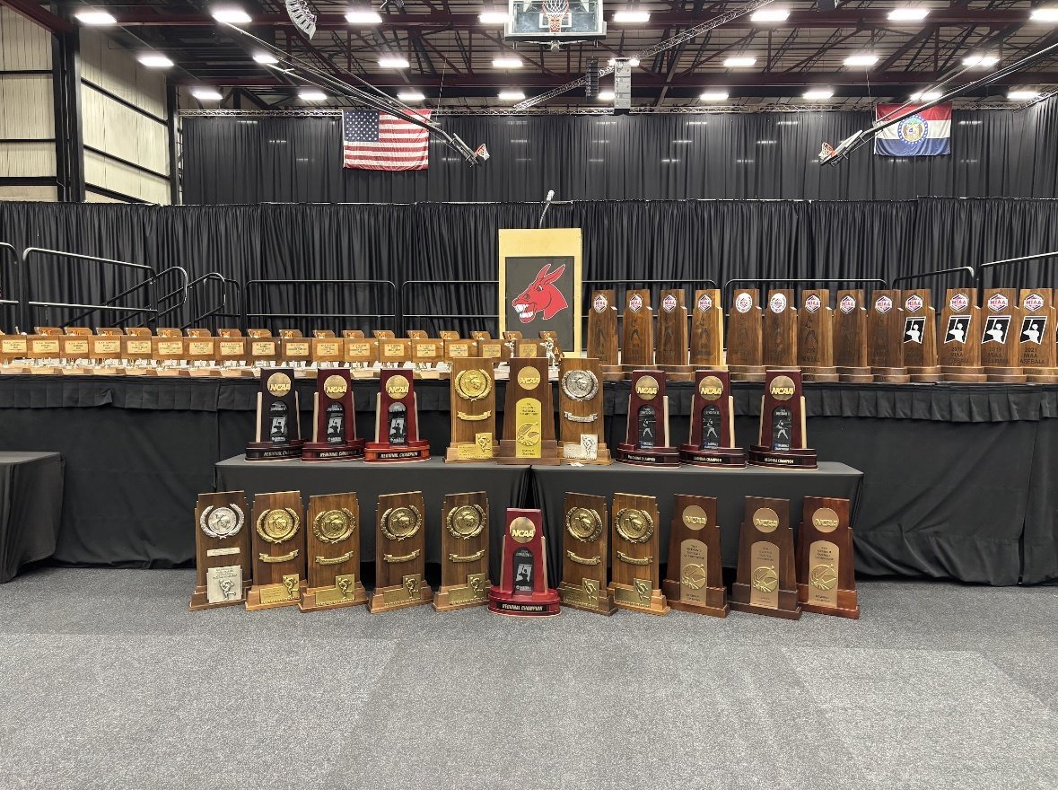 Mules national, regional and MIAA championship trophies lined up in front of the Mules podium